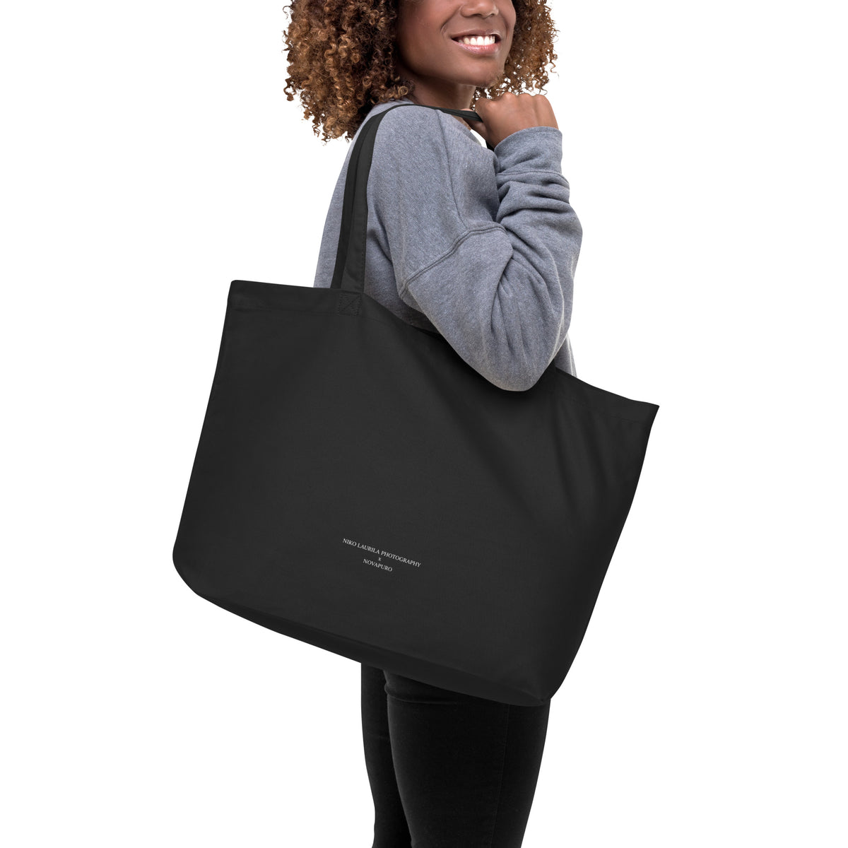 A woman carrying the sustainable black organic cotton tote bag, demonstrating its large everyday capacity and comfortable fit.