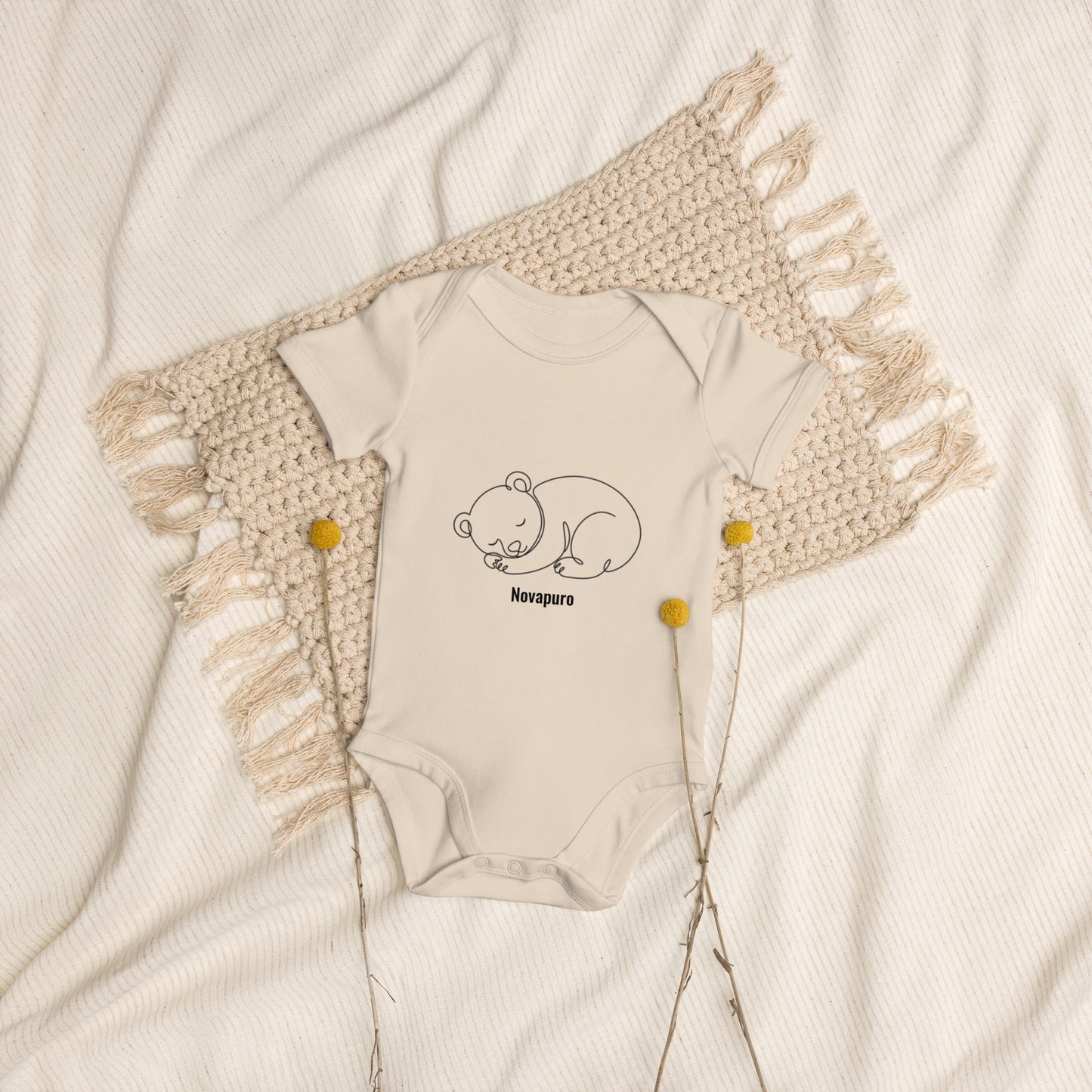 Baby wearing a sand-colored organic cotton bodysuit featuring a minimalist continuous line art of a sleeping bear and the Novapuro logo.