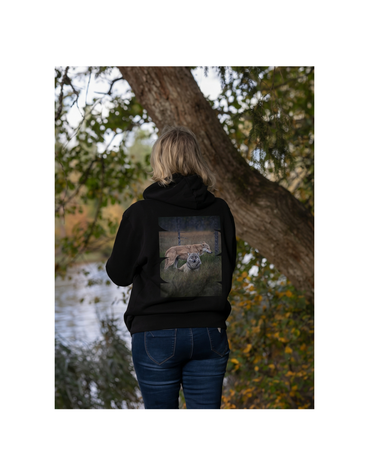 Female model in a forest wearing a black unisex organic cotton hoodie with the 'Leaders of the Pack' wolf duo back print. Sustainable Nordic nature apparel.