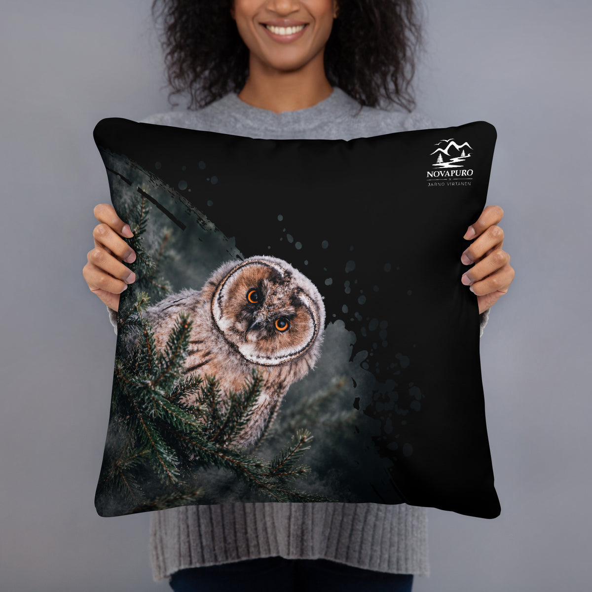 A black accent throw pillow featuring a Nordic long-eared owl chick print by Jarno Virtanen, resting on a bed.