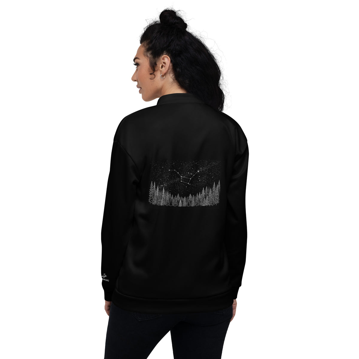 A female model seen from the back wearing a black Novapuro unisex bomber jacket featuring a minimalist white starry night and pine forest graphic.