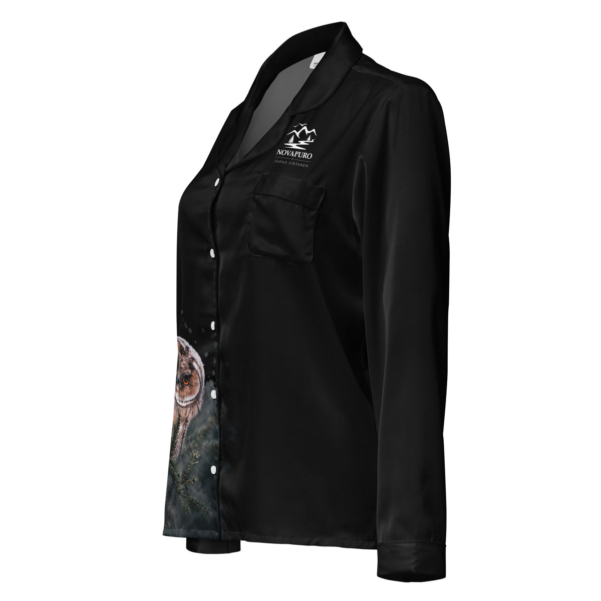 A woman wearing the black Novapuro x Jarno Virtanen long sleeve pajama top featuring a Nordic long-eared owl chick print on the lower side, standing in a cozy room.