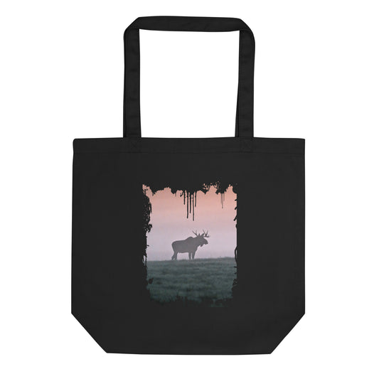 A person carrying a black sustainable organic cotton tote bag, featuring a distressed splash-edge front print of a majestic bull moose by Mikko Monto