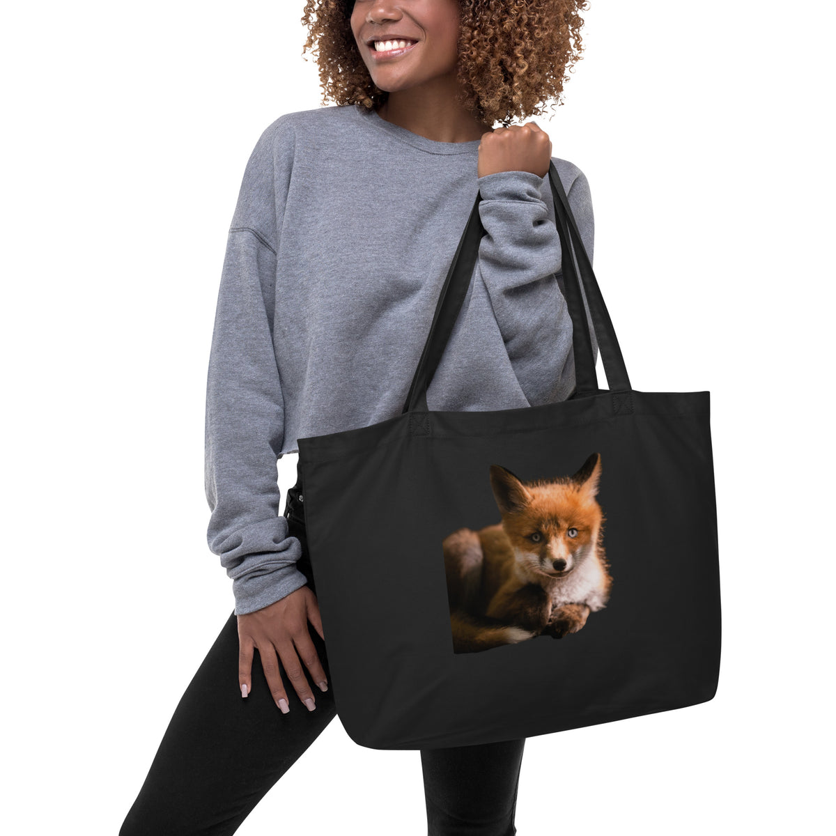 A woman smiling while carrying the black Niko Laurila x Novapuro organic cotton eco tote bag over her shoulder, featuring a striking wild fox print.   