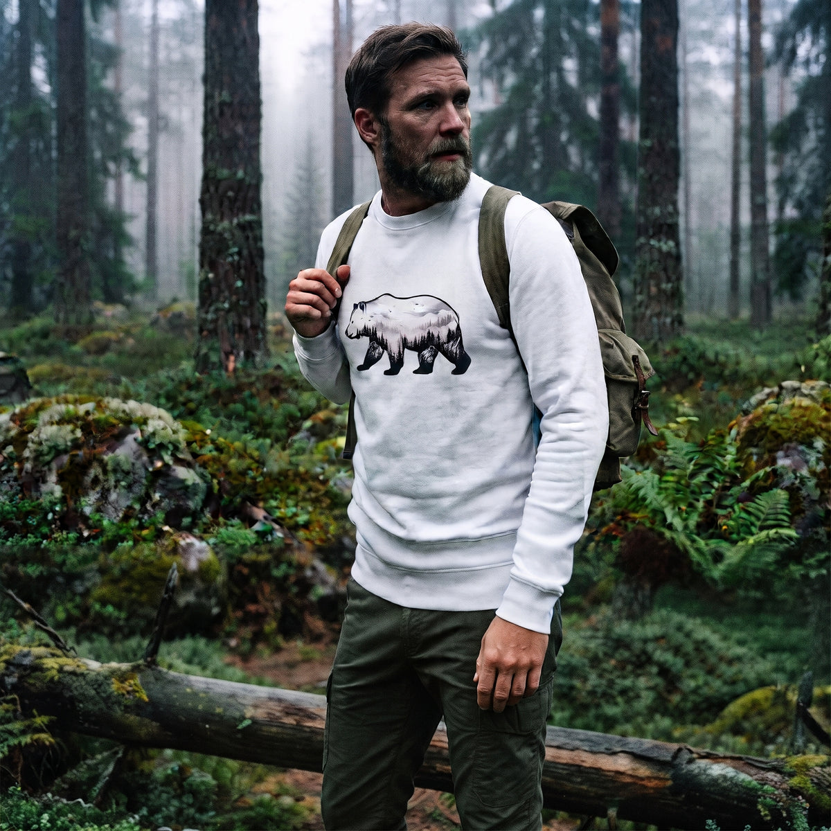 A man standing in a misty Nordic pine forest wearing a sustainable white organic cotton sweatshirt featuring a minimalist bear silhouette design.