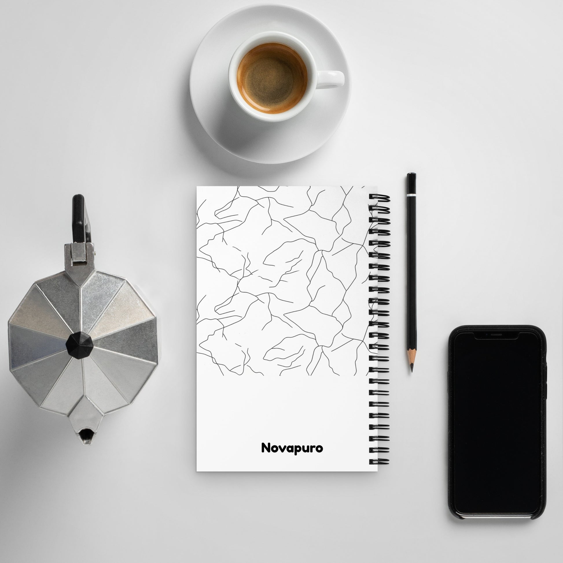 Minimalist spiral notebook with black and white Spring Ice abstract pattern and Novapuro logo on a clean desk with coffee.