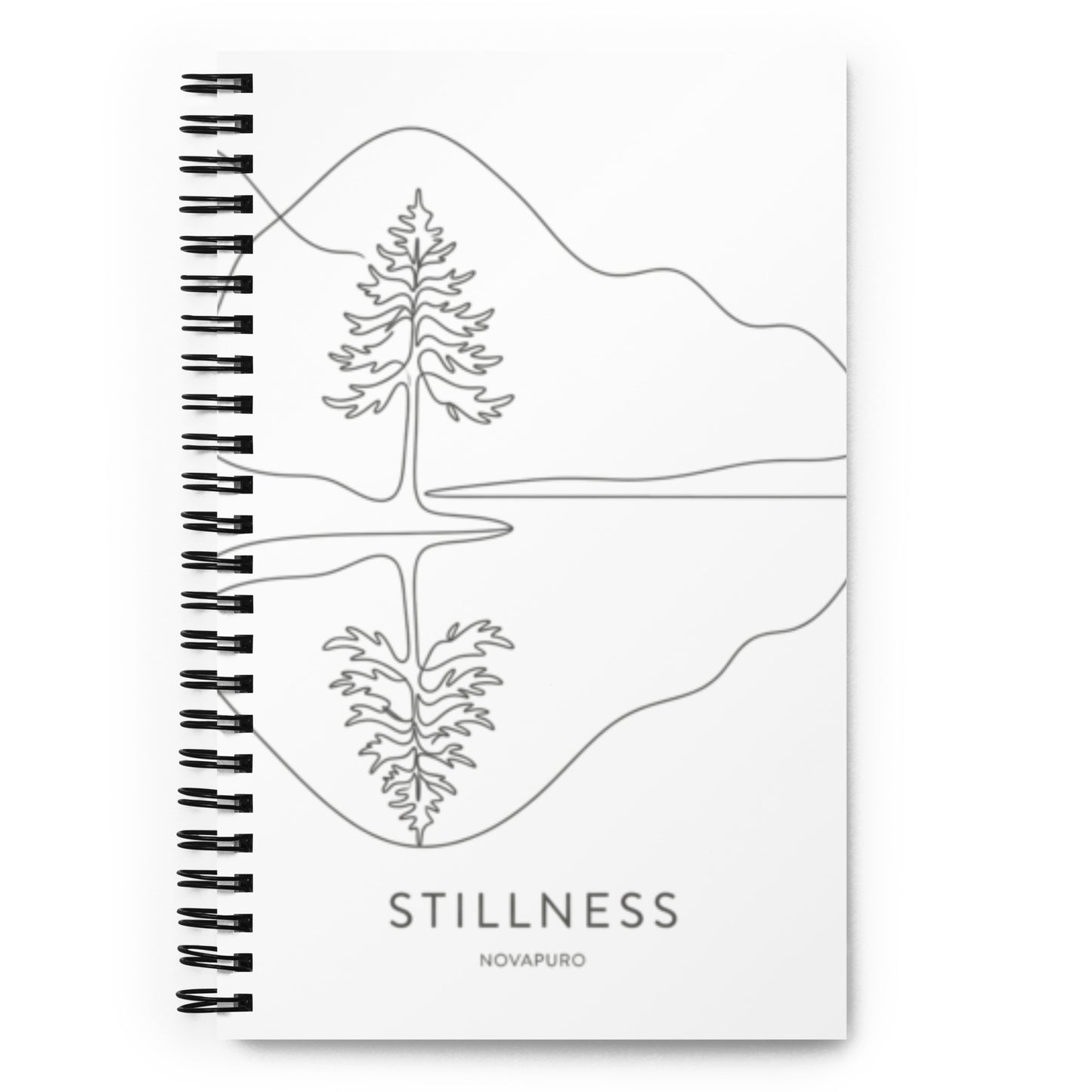 A white spiral-bound notebook laying flat on a desk next to a coffee cup, featuring a minimalist charcoal grey line art illustration of a Nordic lake reflecting a pine tree with the text "STILLNESS".