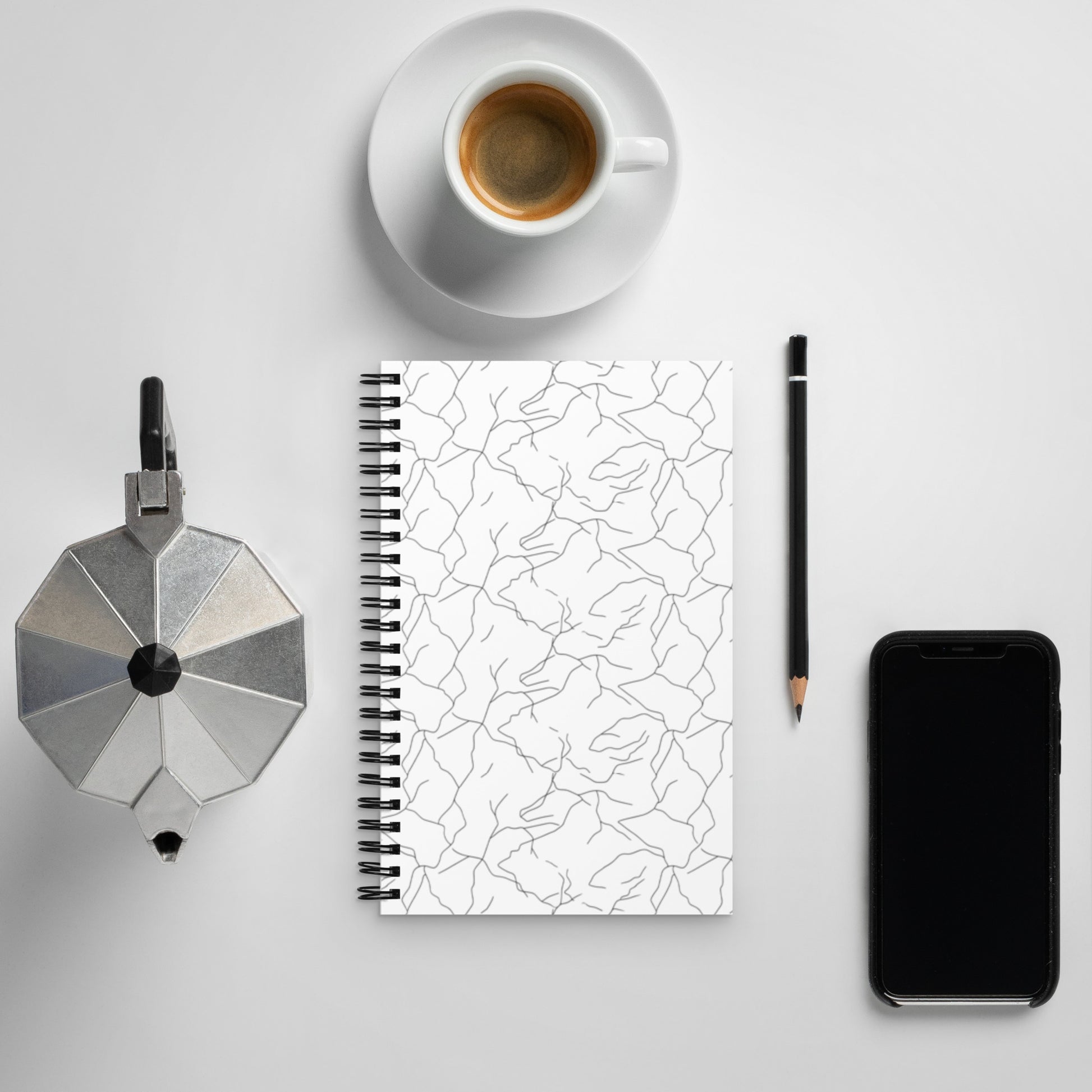Minimalist spiral notebook with black and white Spring Ice abstract pattern and Novapuro logo on a clean desk with coffee.