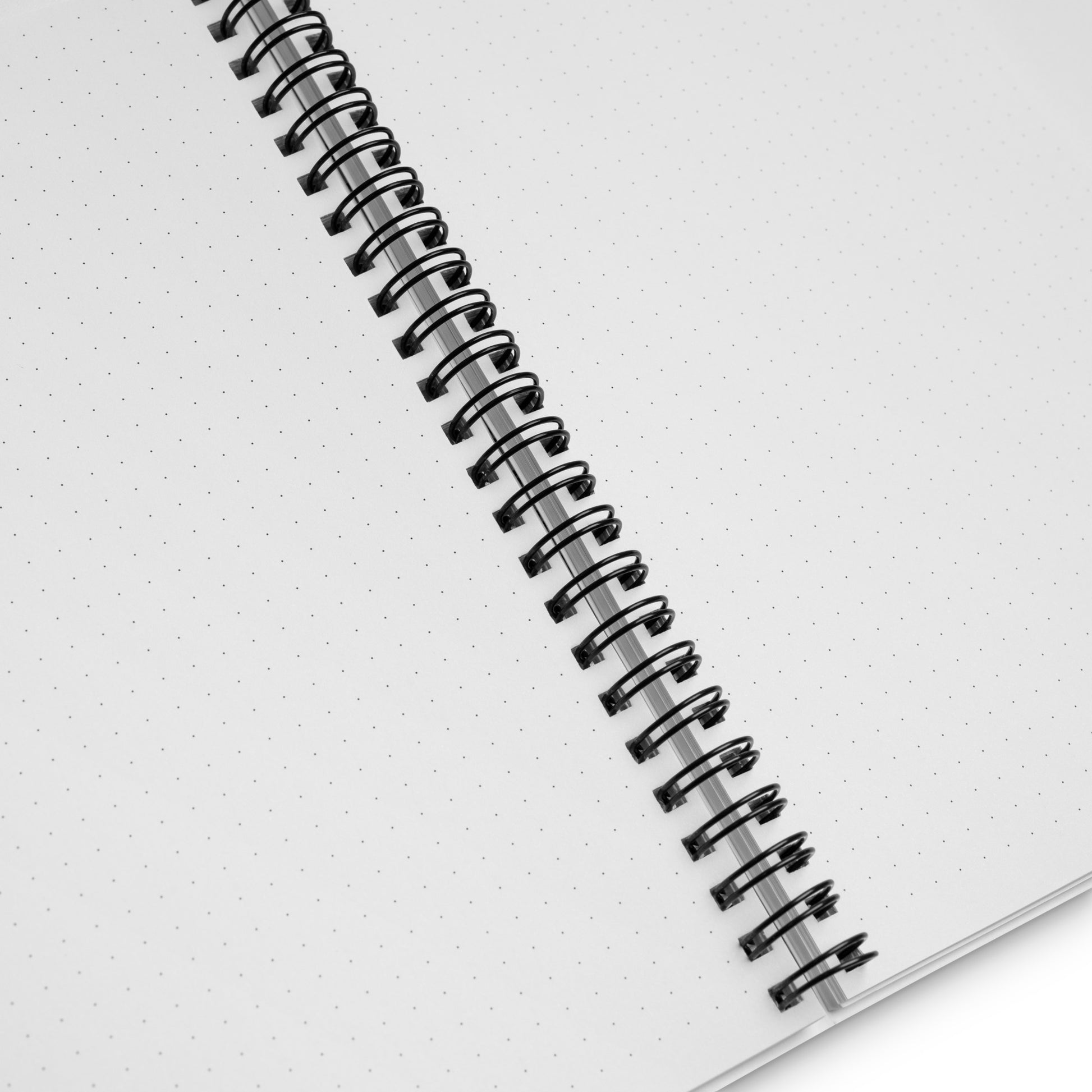 A white spiral-bound notebook laying flat on a desk next to a coffee cup, featuring a minimalist charcoal grey line art illustration of a Nordic lake reflecting a pine tree with the text "STILLNESS".