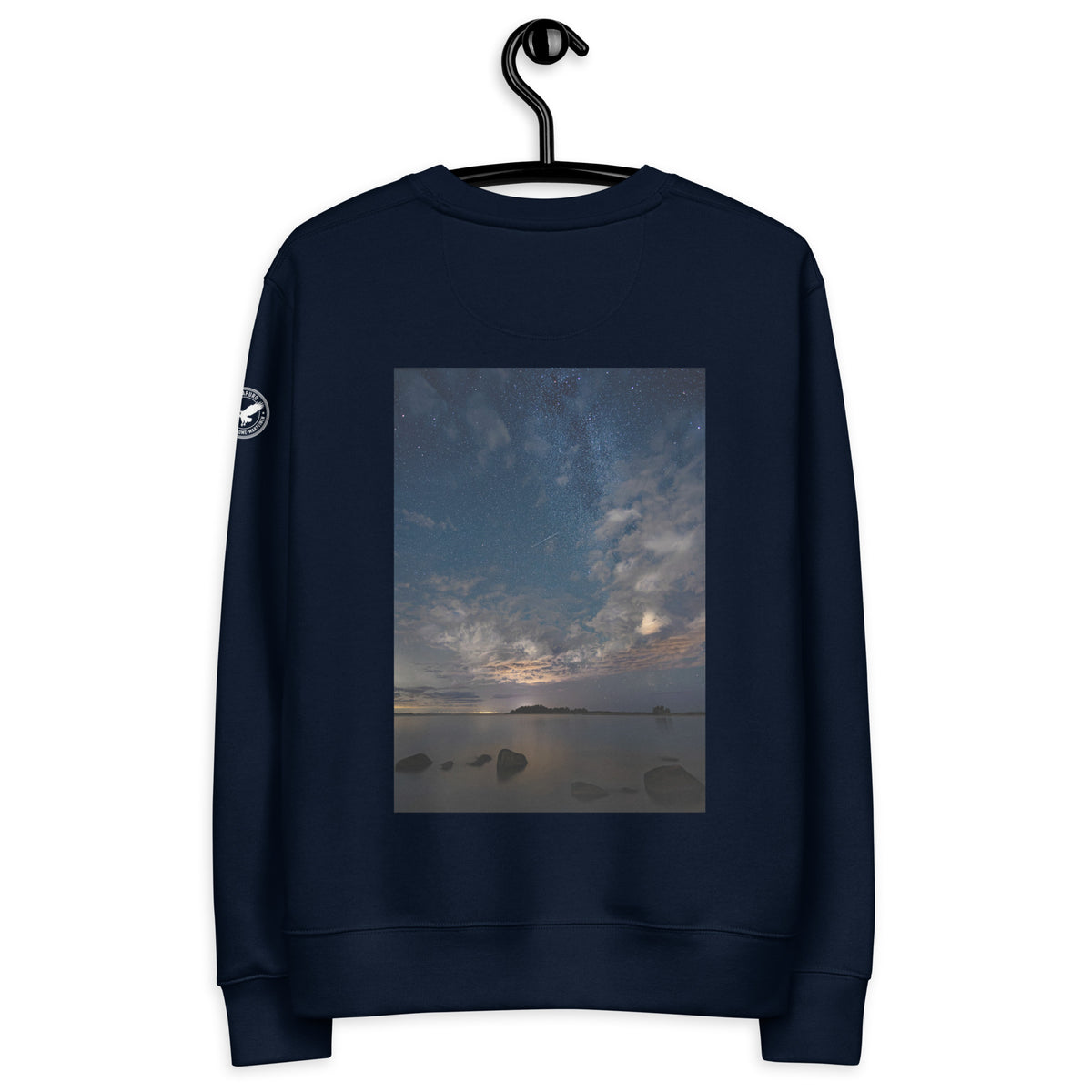 A person wearing the dark navy Novapuro x Annette Thomé-Marttinen 'Nordic Night Sky' organic sweatshirt, featuring a beautiful photograph of a starry night and a shooting star over a calm lake.
