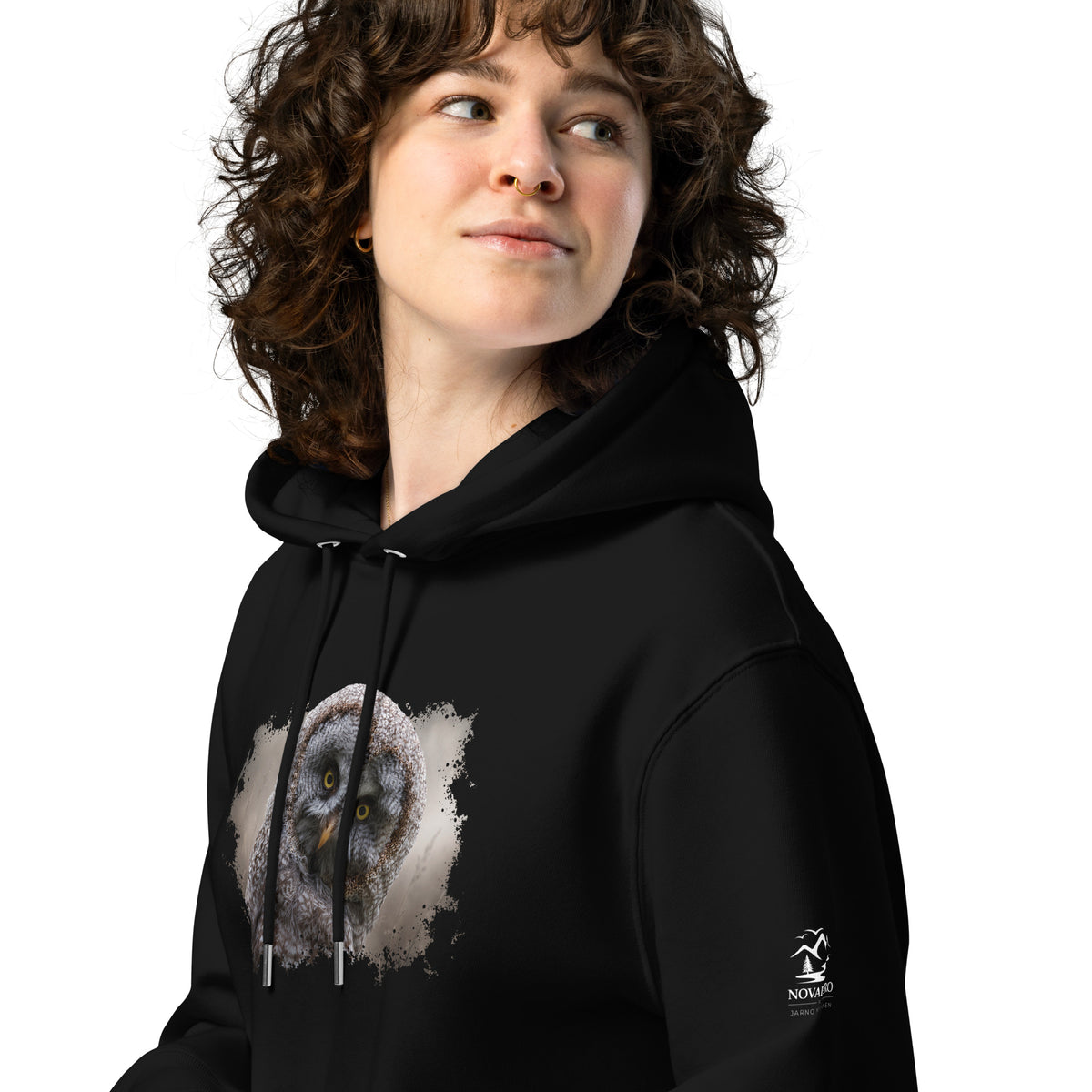 Woman wearing a black Novapuro organic cotton hoodie featuring a Great Grey Owl wildlife photograph by Jarno Virtanen. Sustainable, ethical Nordic apparel.