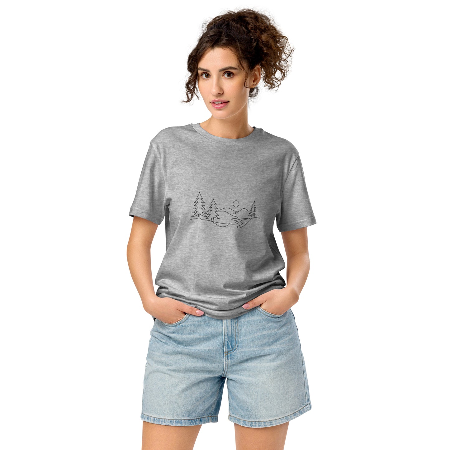 A person wearing a grey unisex 100% organic cotton t-shirt featuring a minimalist continuous line art illustration of a Nordic pine forest and mountains.