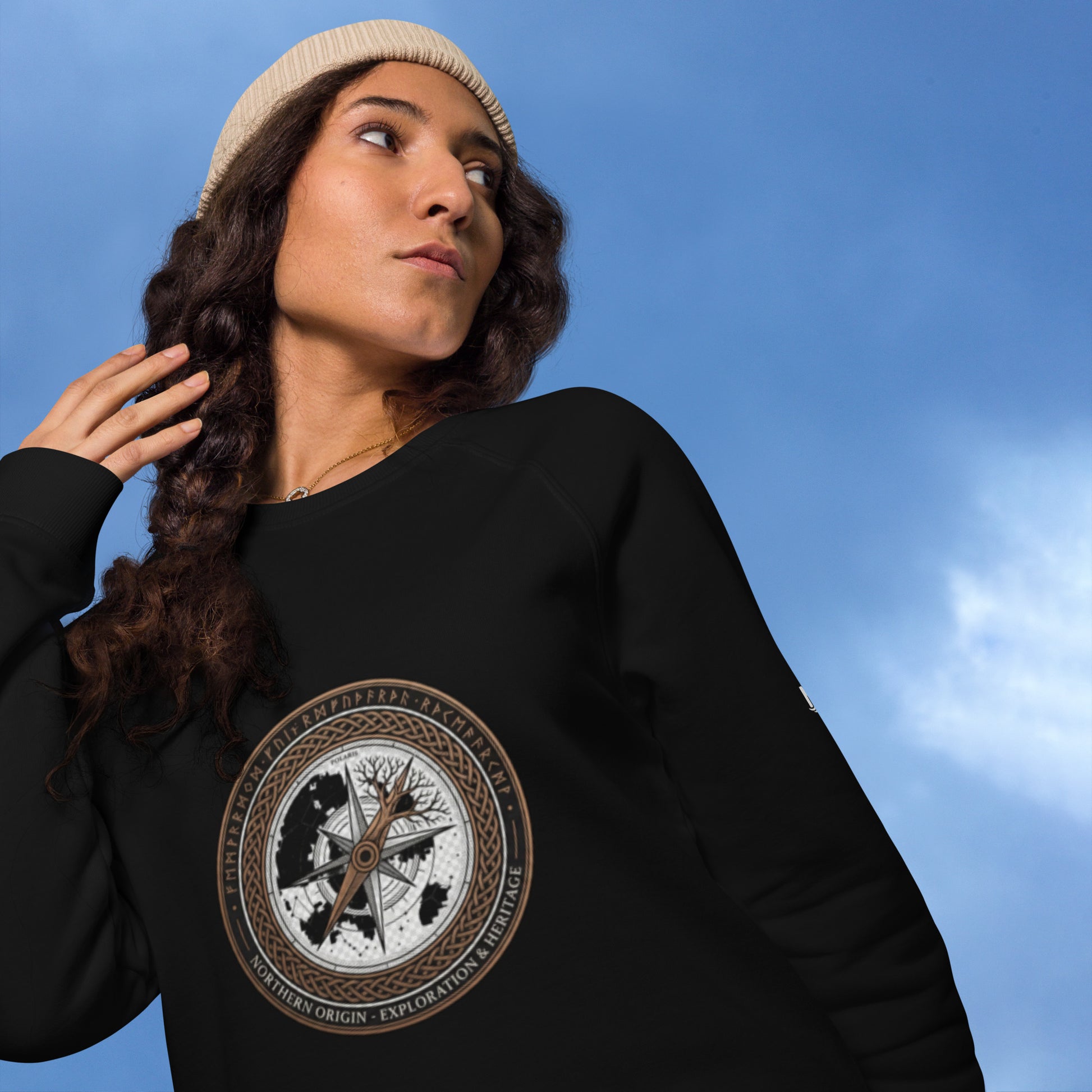 A model wearing a black unisex organic raglan sweatshirt featuring a vintage circular compass and Nordic tree emblem with the text Northern Origin.