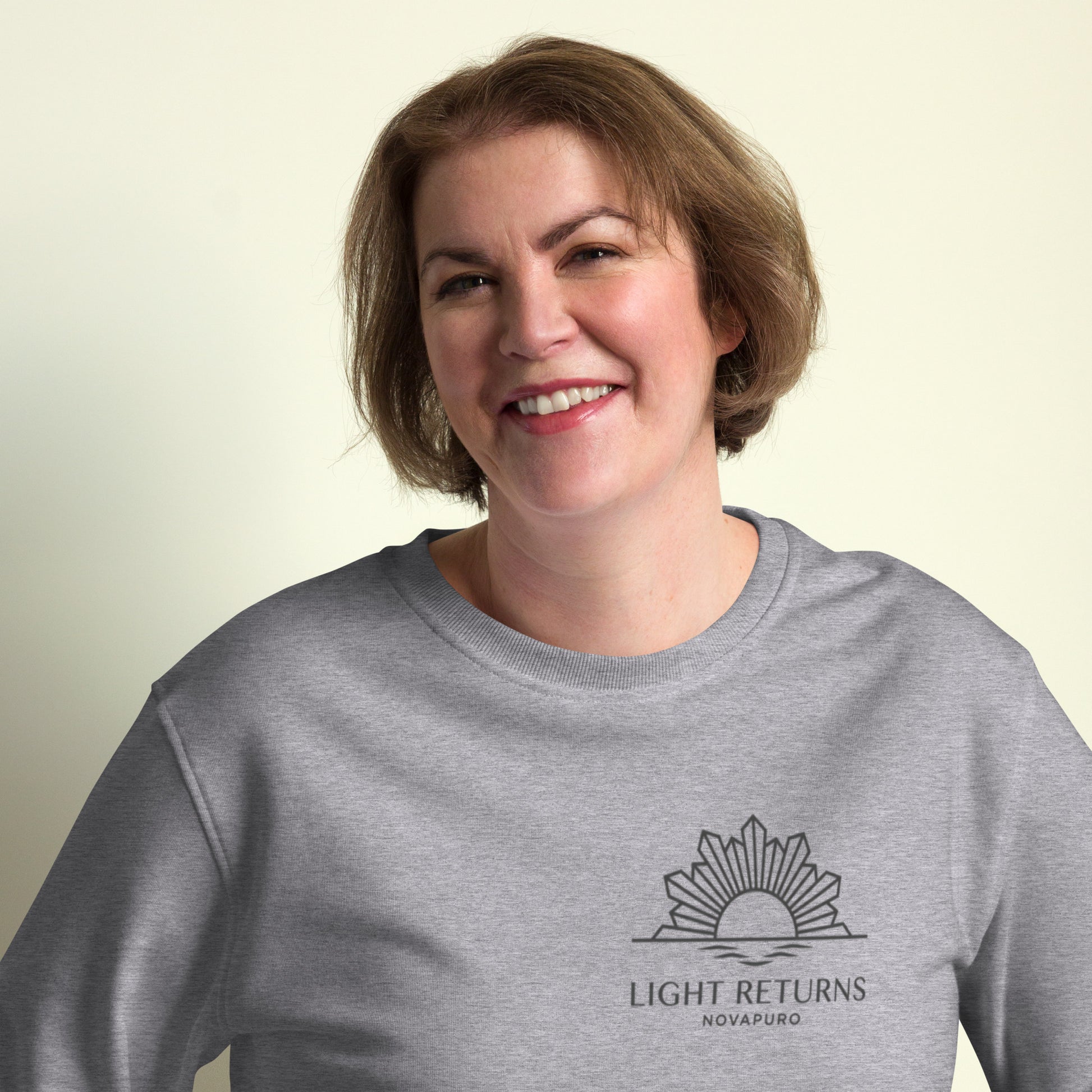 Minimalist sun graphic with 'Light Returns Novapuro' text on a grey or white eco-friendly organic cotton sweatshirt.