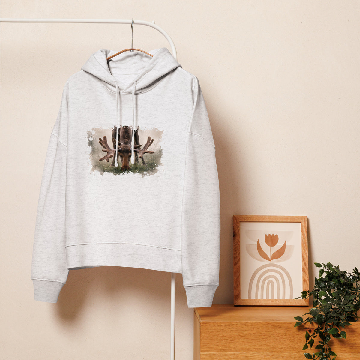 Nordic lifestyle view of the women's white organic moose hoodie hanging on a clothing rack in a cozy room.