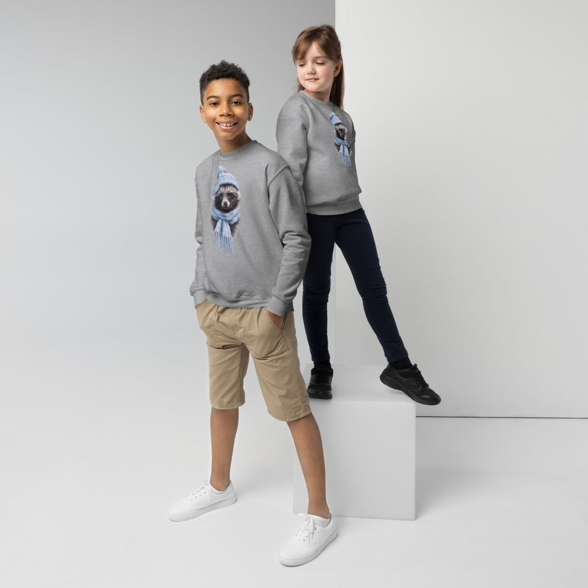 Two children modeling the grey Winter Raccoon youth crewneck sweatshirt by Annette Thome Marttinen x Novapuro.
